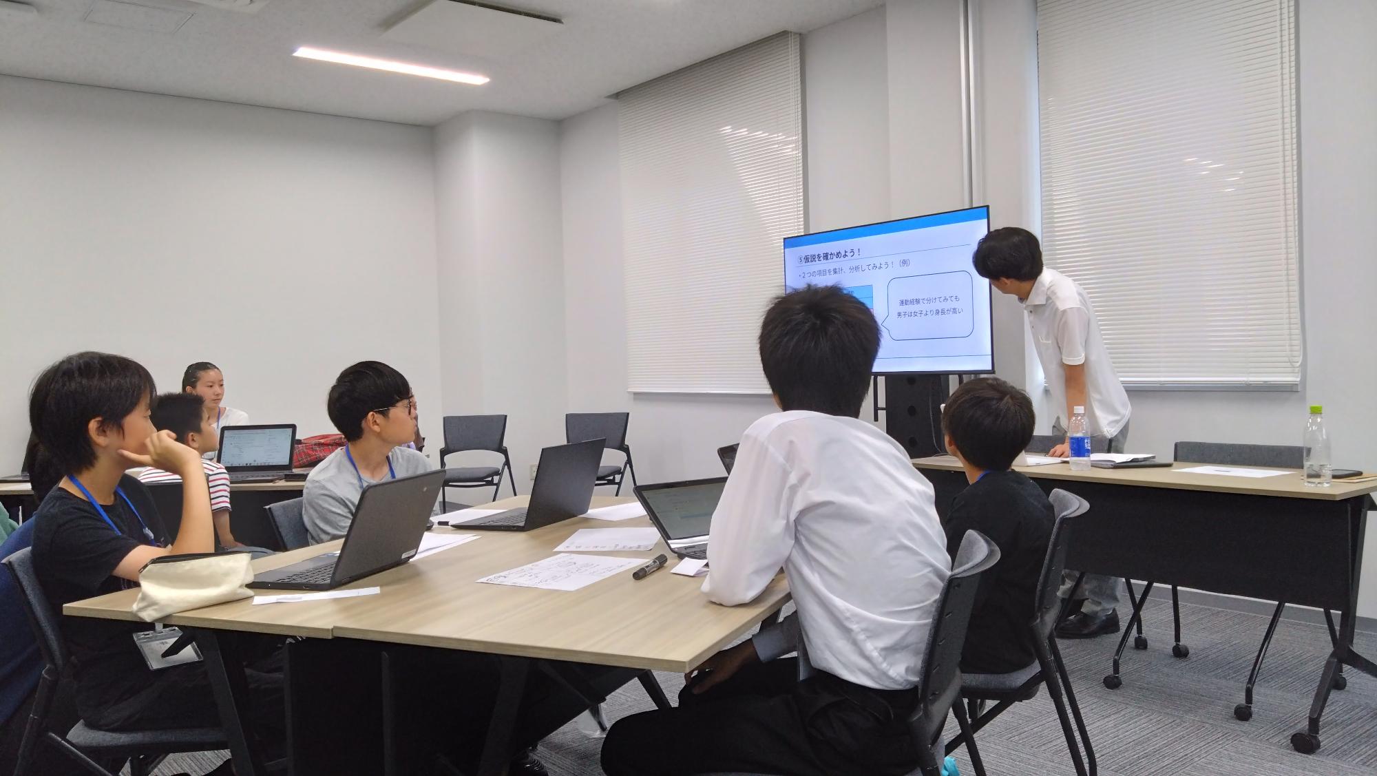 一人一台パソコンの前に座って先生の話を真剣に聞く子どもたち