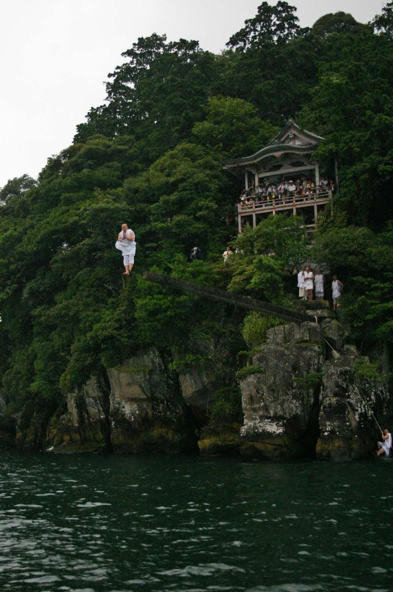 あごの下で両手を合わせた修行僧がまさに竿から湖面へとまっすぐに足から飛び込んだ写真