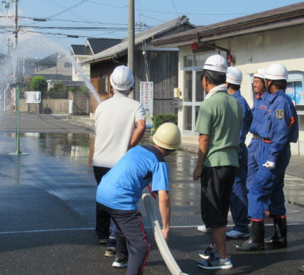 防災訓練で一般市民が消防隊員らの指導を受けながら放水を行っている様子の写真