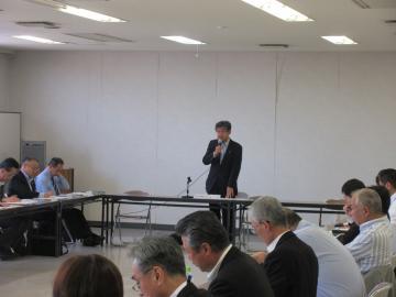 近江八幡市防災会議にて、四角く並べられた机に座る男性参加者を前にマイクを手に話す市長の写真