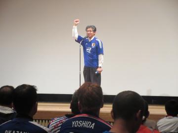 サッカー日本代表チームの壮行試合のパブリックビューイングにて、着席する参加者を前に日本代表のユニフォーム姿で話す市長の写真