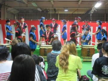 第31回沖島町夏祭りにて、沖縄太鼓を披露するこどもたちと、座って見守る大人たちの写真