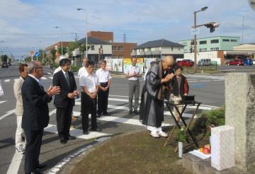七塚碑前にて手を合わせる僧侶とその後ろで合掌をする市長ら職員の写真