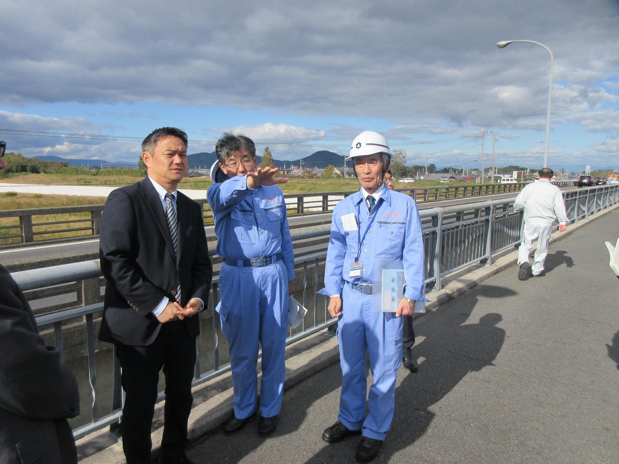 青い作業着を着た市長が、同じく青の作業着を着た男性やスーツの男性と河川視察を行っている写真