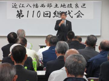 西部土地改良区総代会にて、着席する参加者の前で話す市長の写真