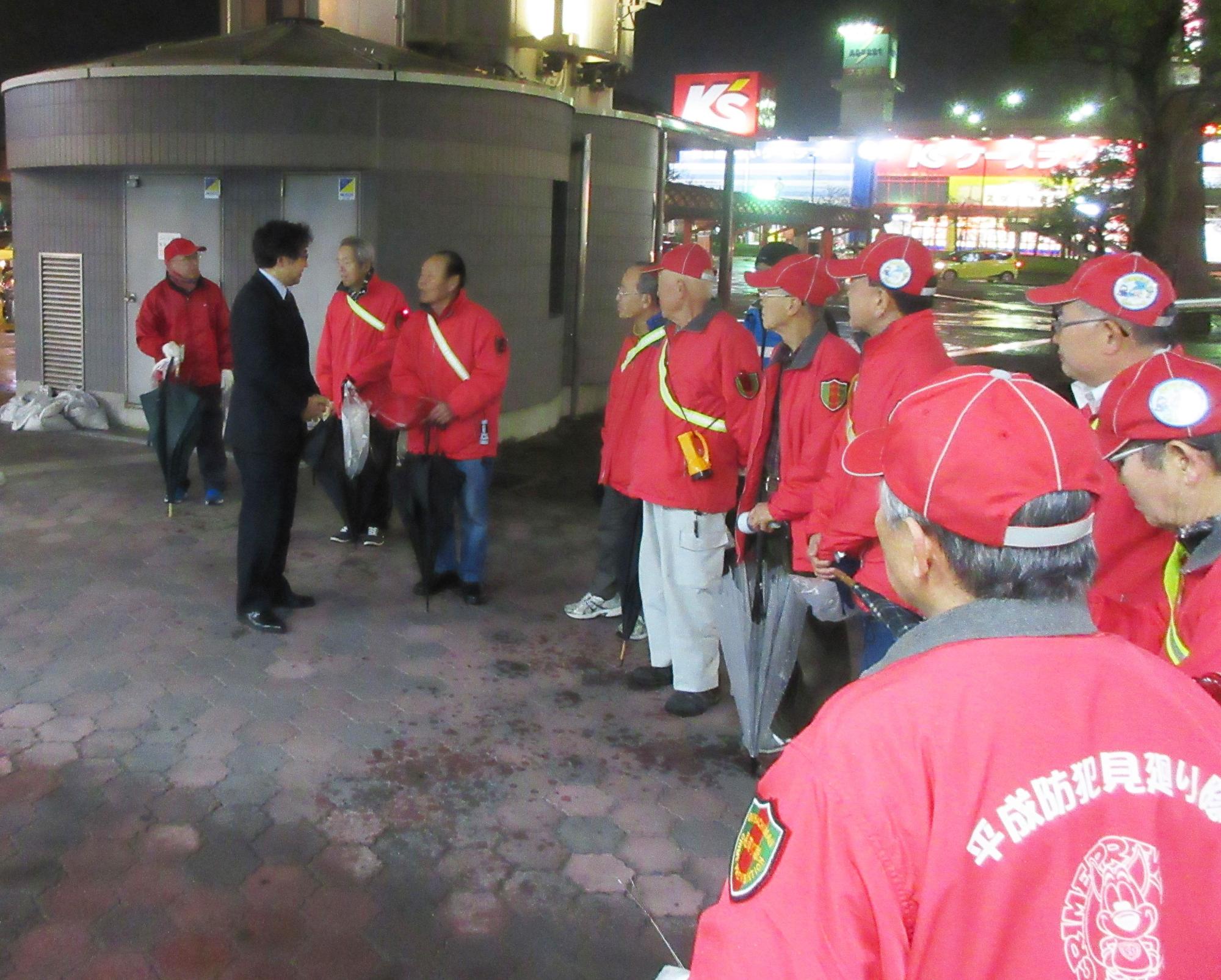 赤いジャンパーを着た平成防犯見廻り隊の男性らを前に激励を行う市長の写真