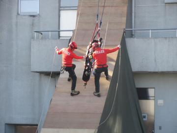 急斜面をロープ頼りに降りながら救護活動の訓練を行う、オレンジの服を着た2名の消防隊員の写真