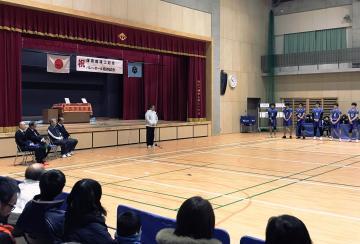 岡山小学校新体育館竣工記念(杮落とし)事業にて、バレーボールのユニフォームを着て並ぶ選手立ちの前で話す市長の写真