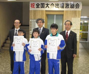 全国大会出場の成賞状を胸に掲げる男の子3人と、その後ろに立つ市長とスーツの男性二人の写真