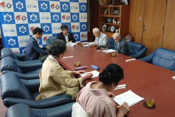 八幡教育会館評議会にて、机に置かれた資料を読む参加者と市長の写真