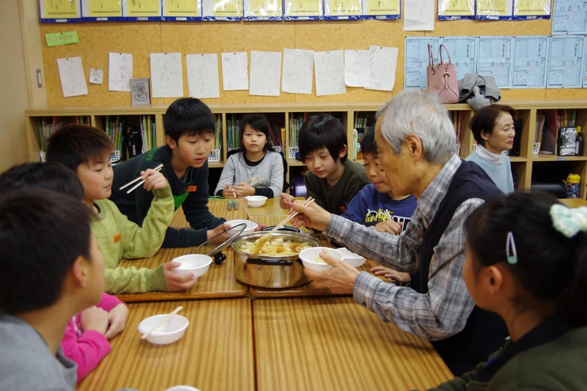 桐原小学校大根パーティー：机の上にあるおでんを子供たちと食べている大人の写真