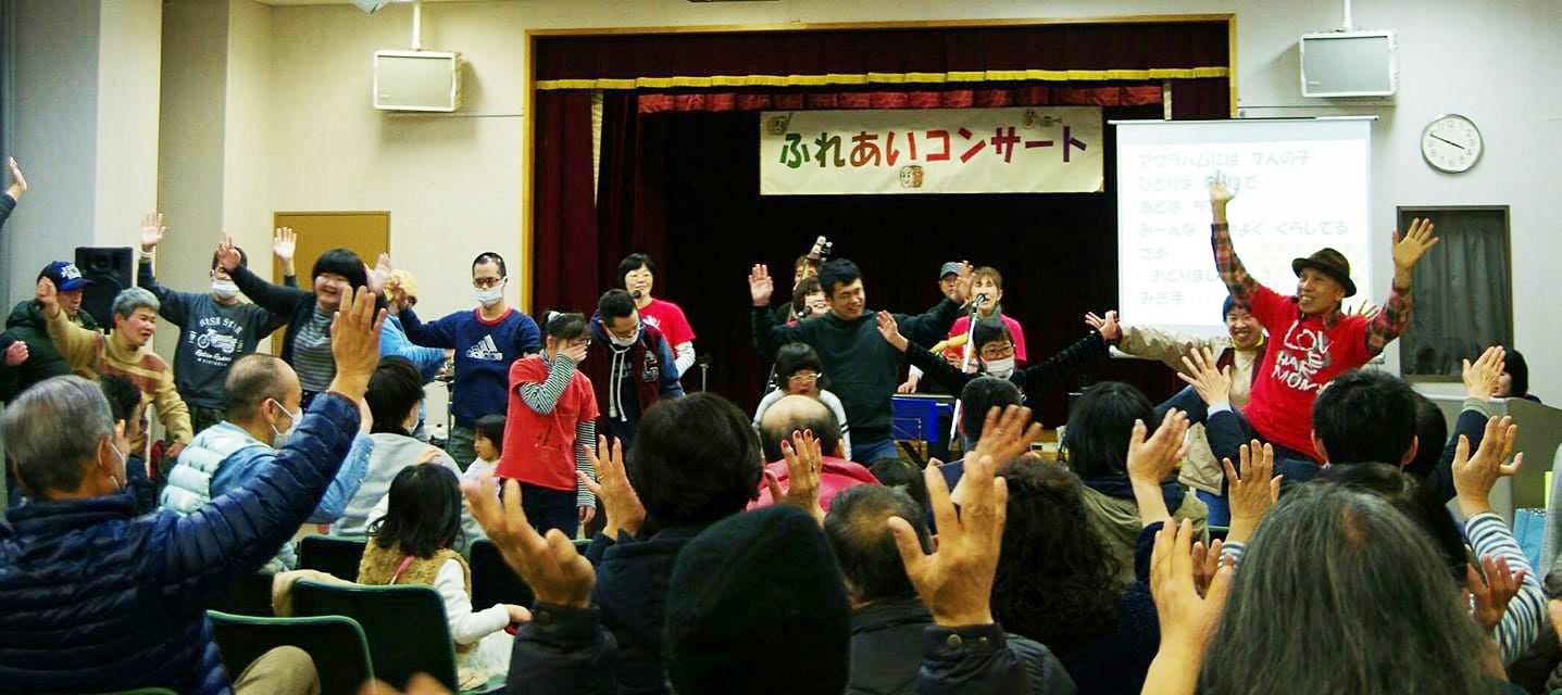 ふれあいコンサート：室内にて手を挙げて踊っている演奏者たちと観客たちの写真