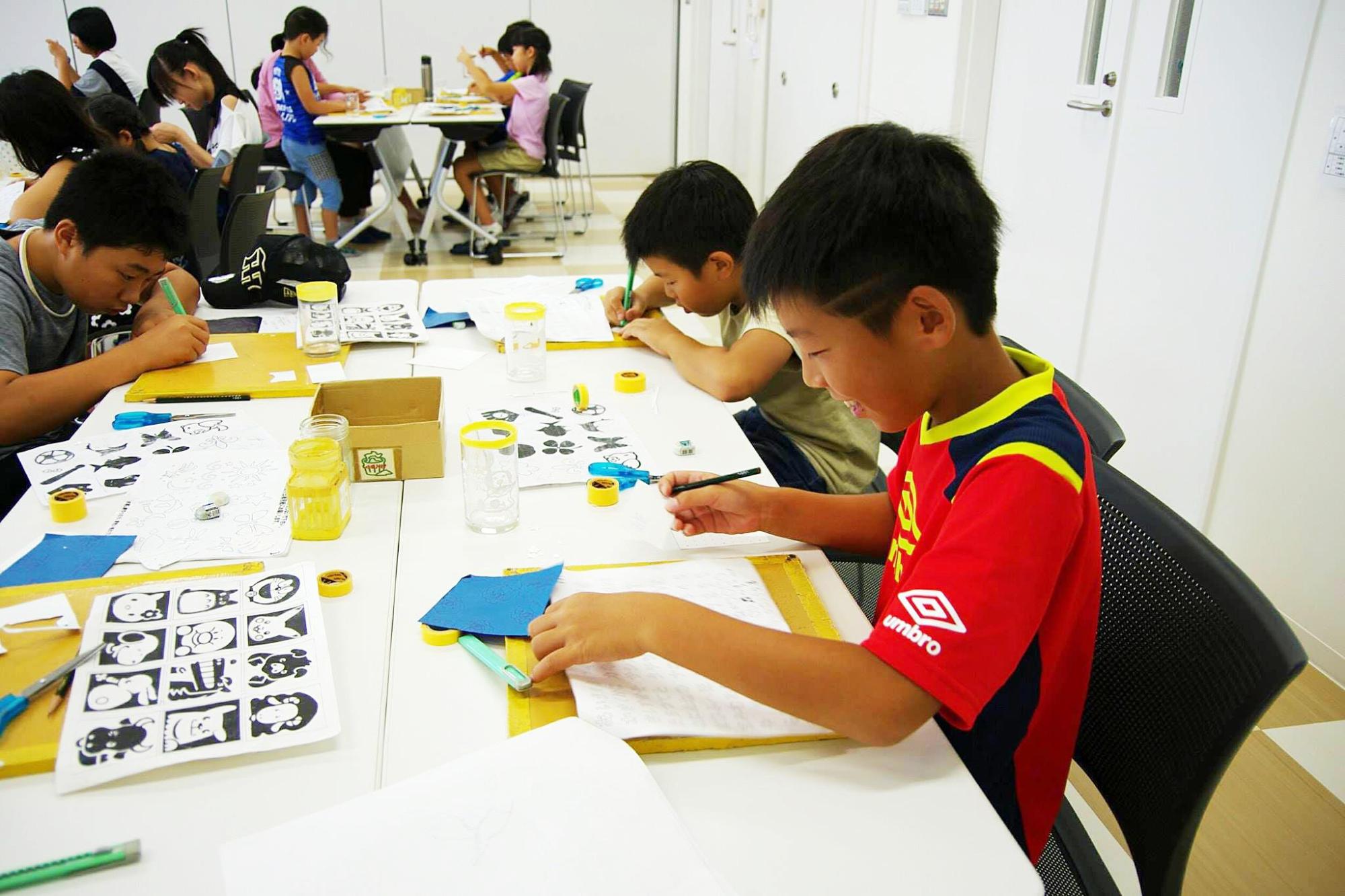 サンドブラスト体験：机に向かって作品を作成している子供たちの写真
