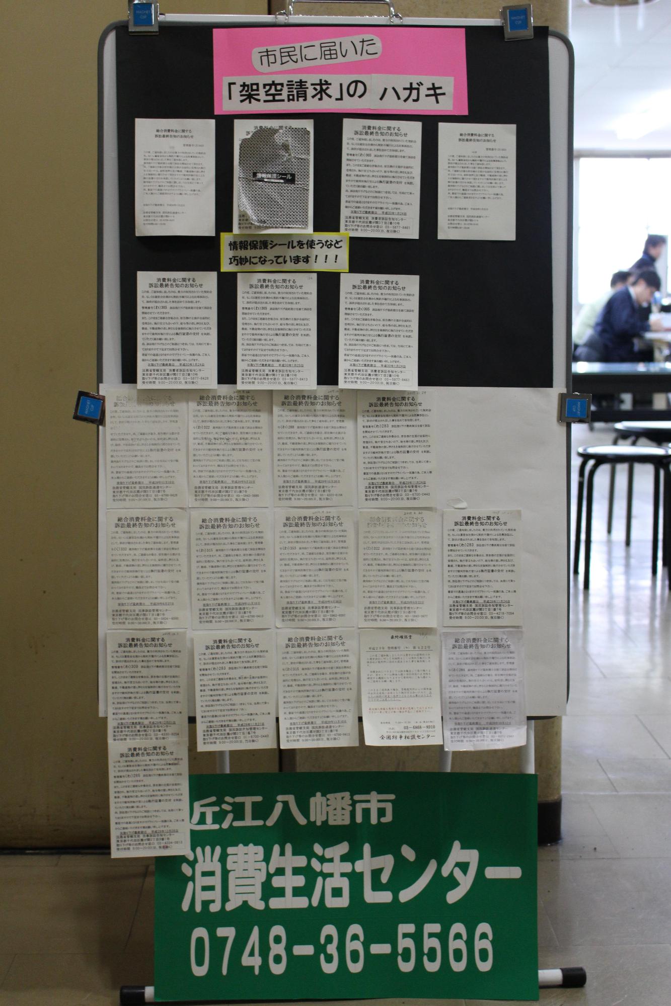 架空請求のハガキを大きくコピーした紙(十数枚)の下に、消費生活センターの電話番号が大きく書かれている掲示板の写真