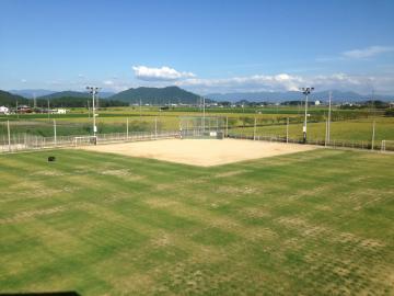 金田小学校の芝生の校庭と一角の野球場、彼方の山並みを望む写真