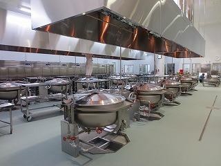 大きな釜がに列に設置されている調理室の写真