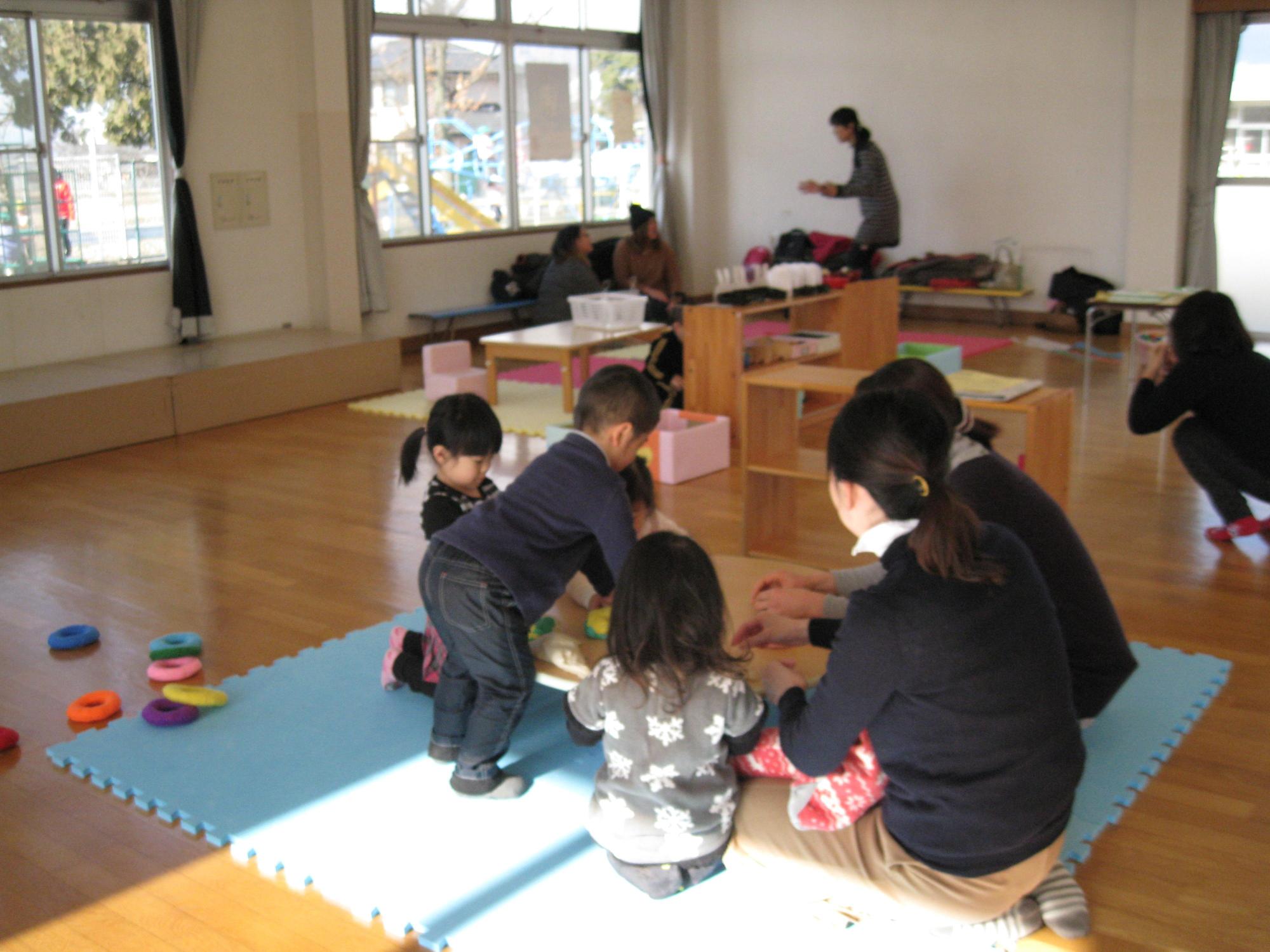 教室で数人の子供たちと大人がおもちゃを使って遊んでいる写真