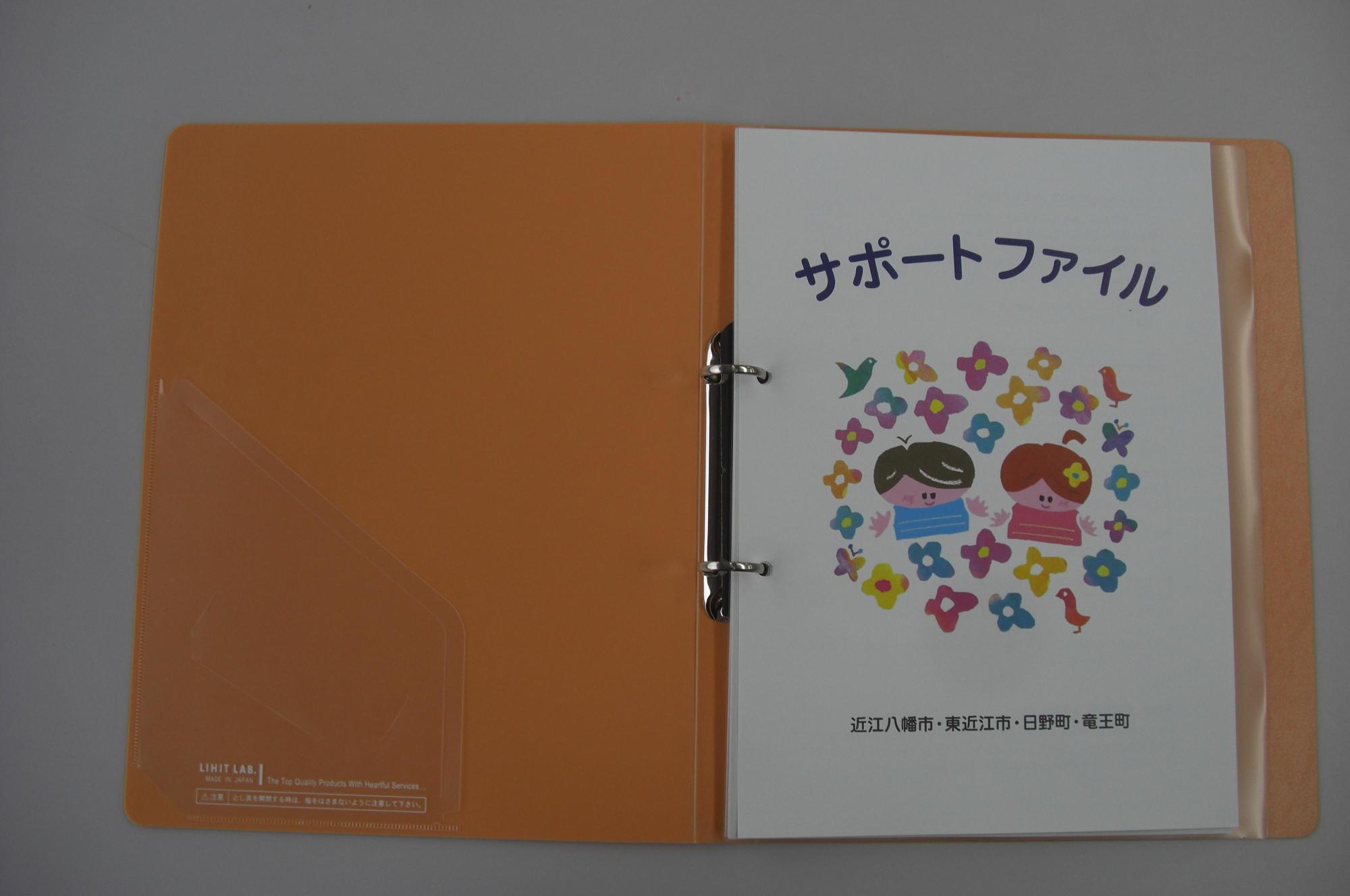 サポートファイルの文字と鳥・花・子供のイラストの描かれた資料がはさまっている、開いた状態の黄色いファイルの写真