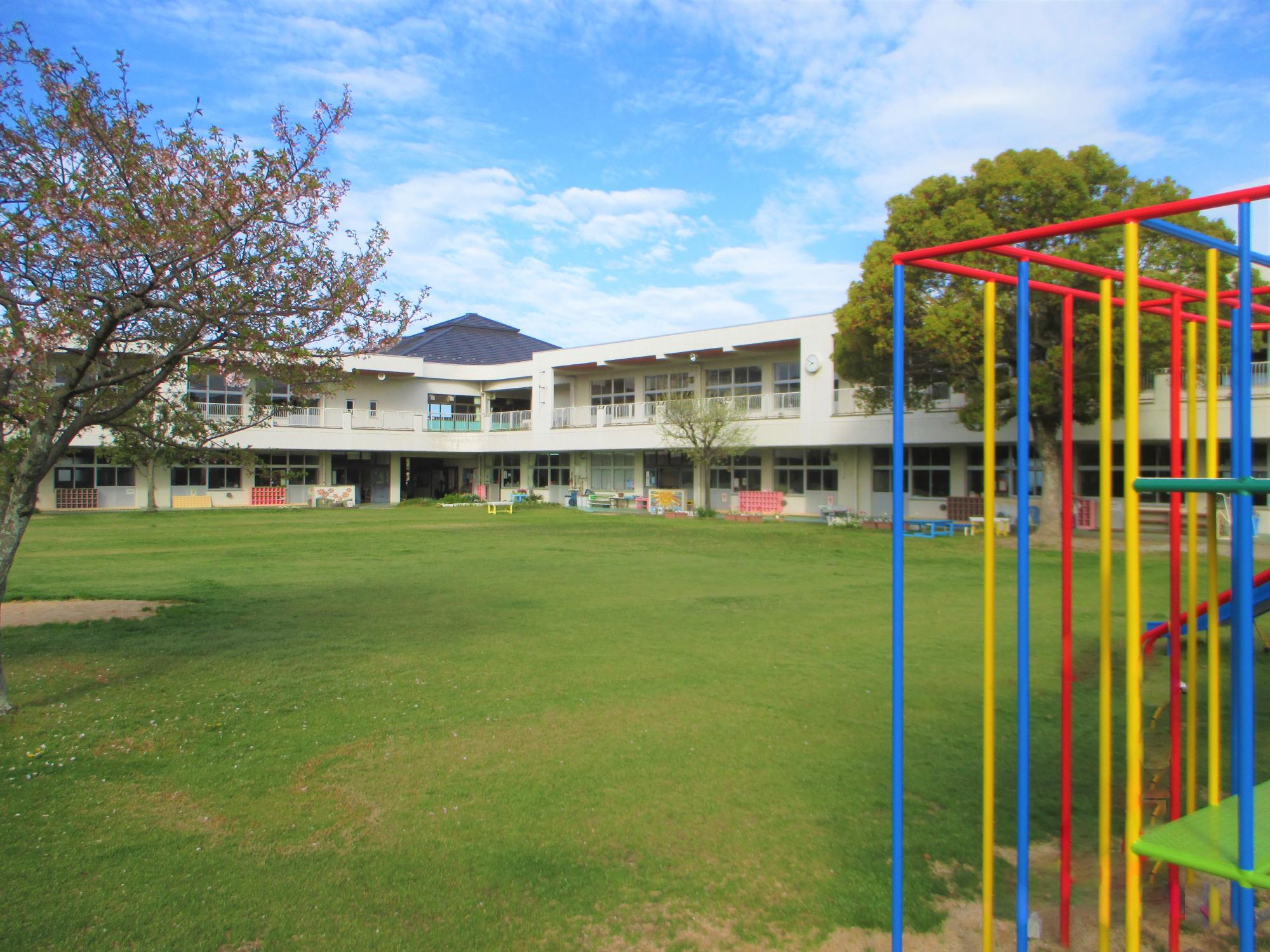 新しい大型遊具が右手前に映り、広い園庭の金田幼稚園の外観の写真